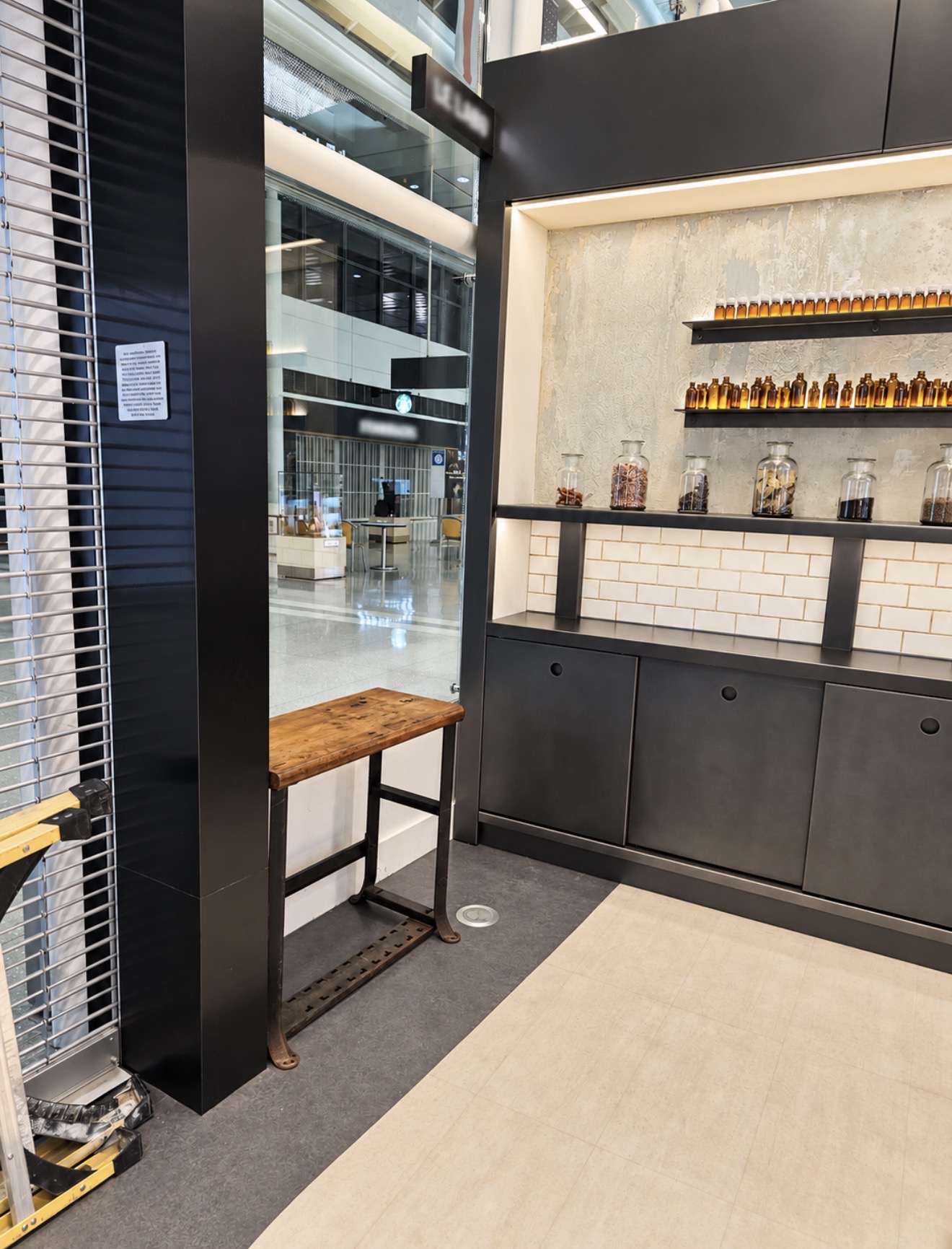 Illuminated shelving unit with amber bottles and dark cabinets beside a timber bench