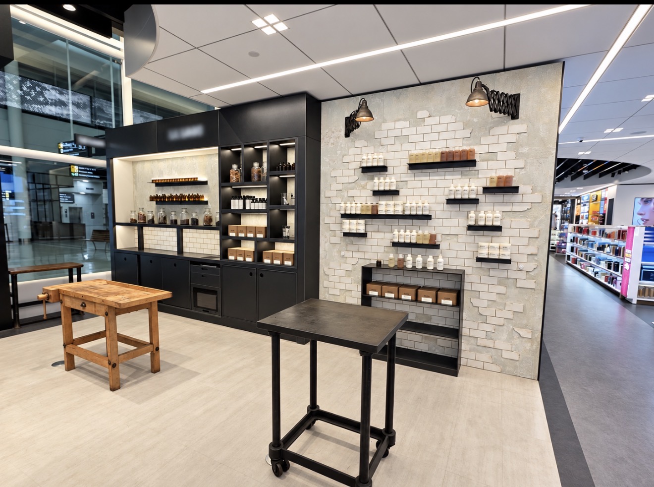 Retail space with dark cabinetry, illuminated shelving, tiled display wall and timber workbench