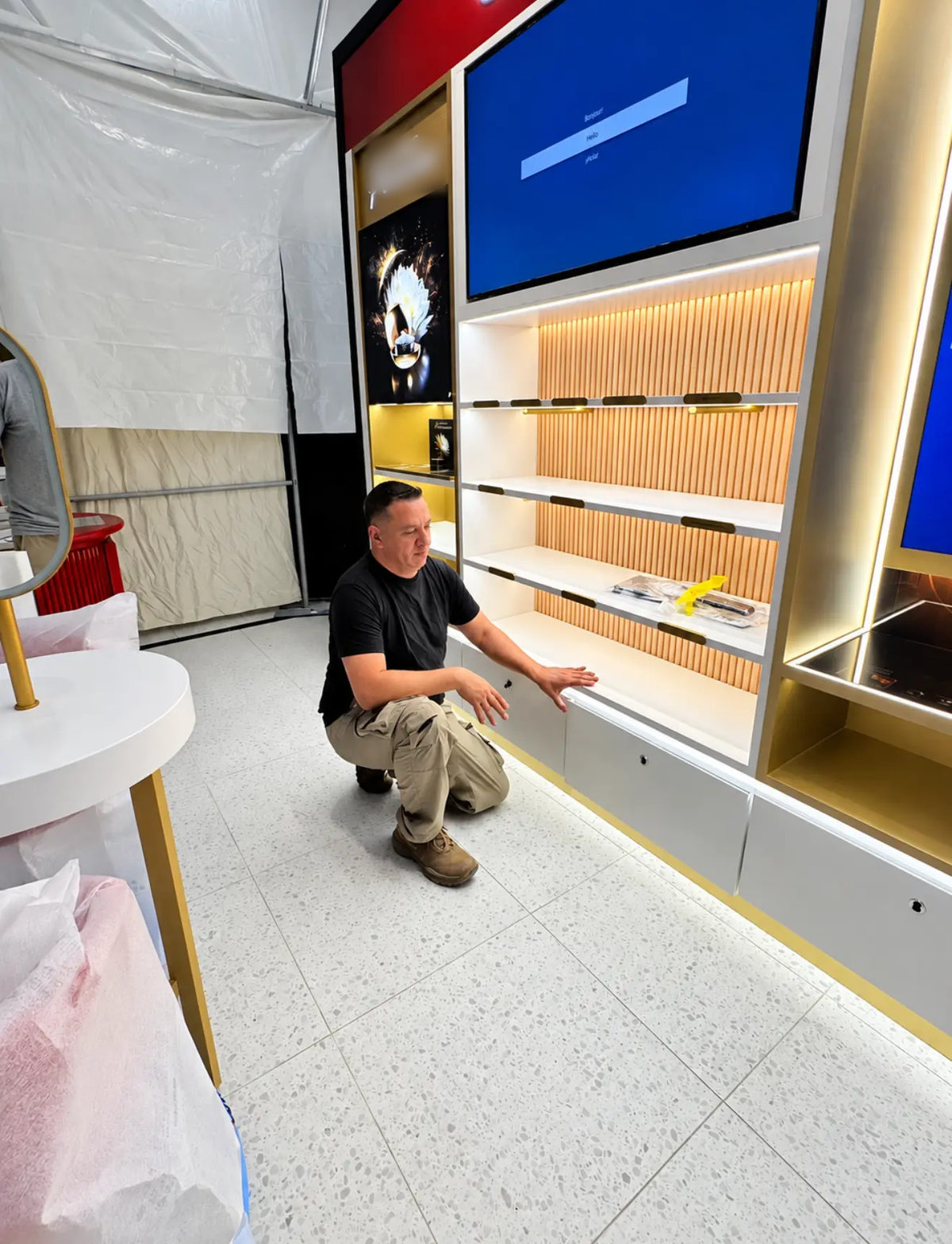 Installer crouching in front of an illuminated shelving unit in a beauty retail space